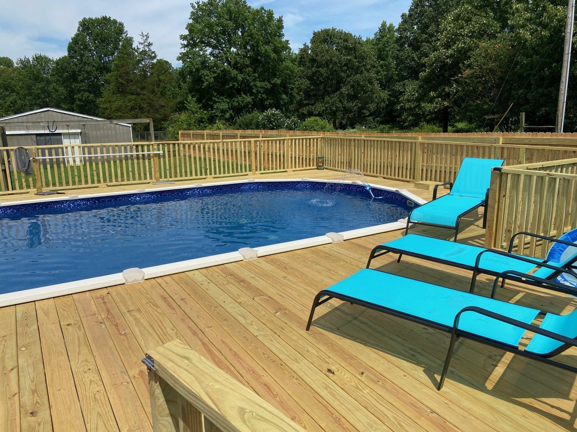 A large swimming pool is surrounded by a wooden deck with blue lounge chairs.