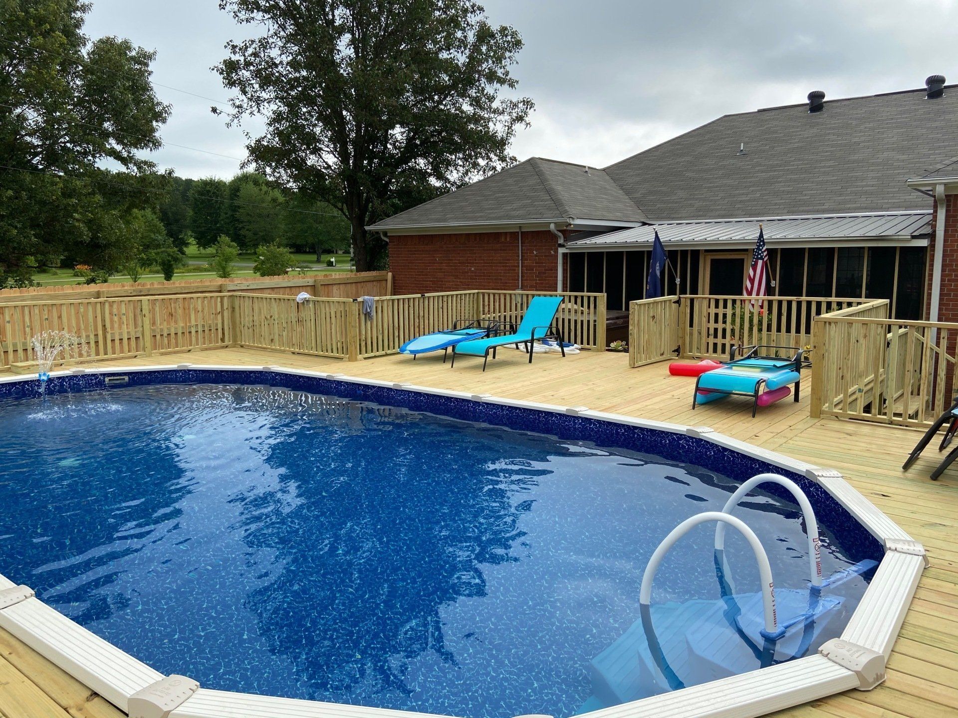 A large swimming pool with a wooden deck in front of a house.