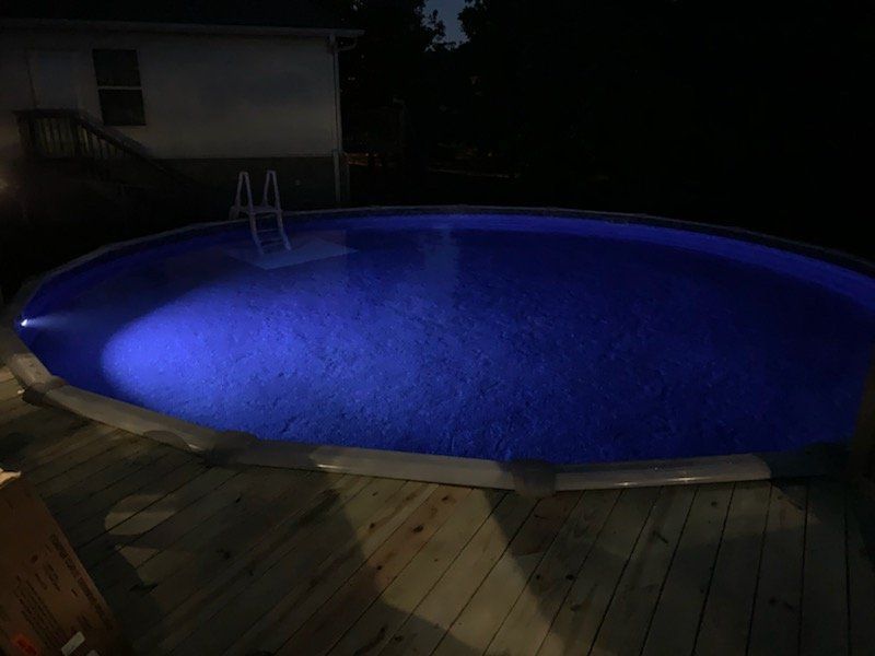 A swimming pool is lit up at night with blue lights.