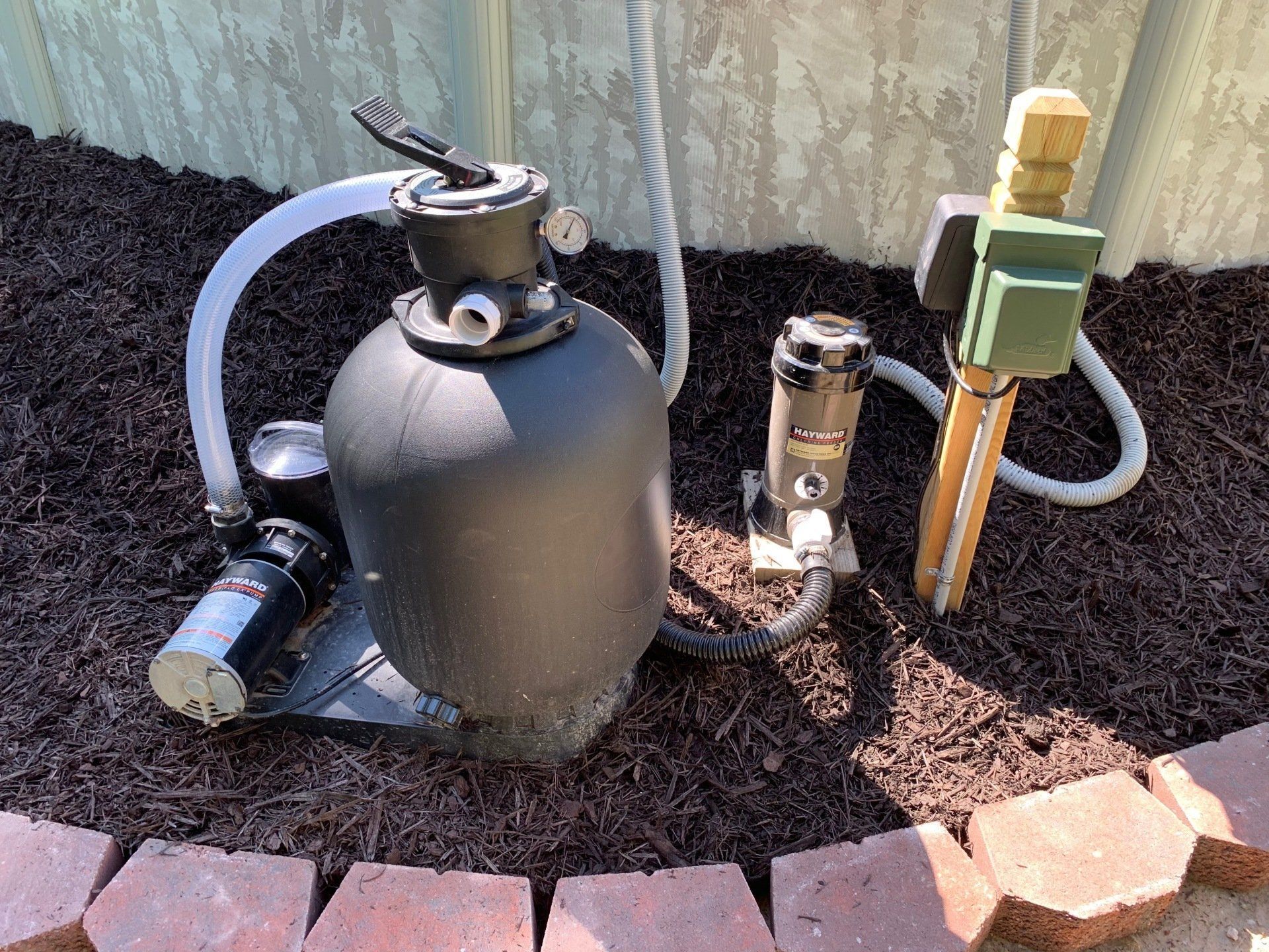A black sand filter is sitting on top of a pile of mulch.