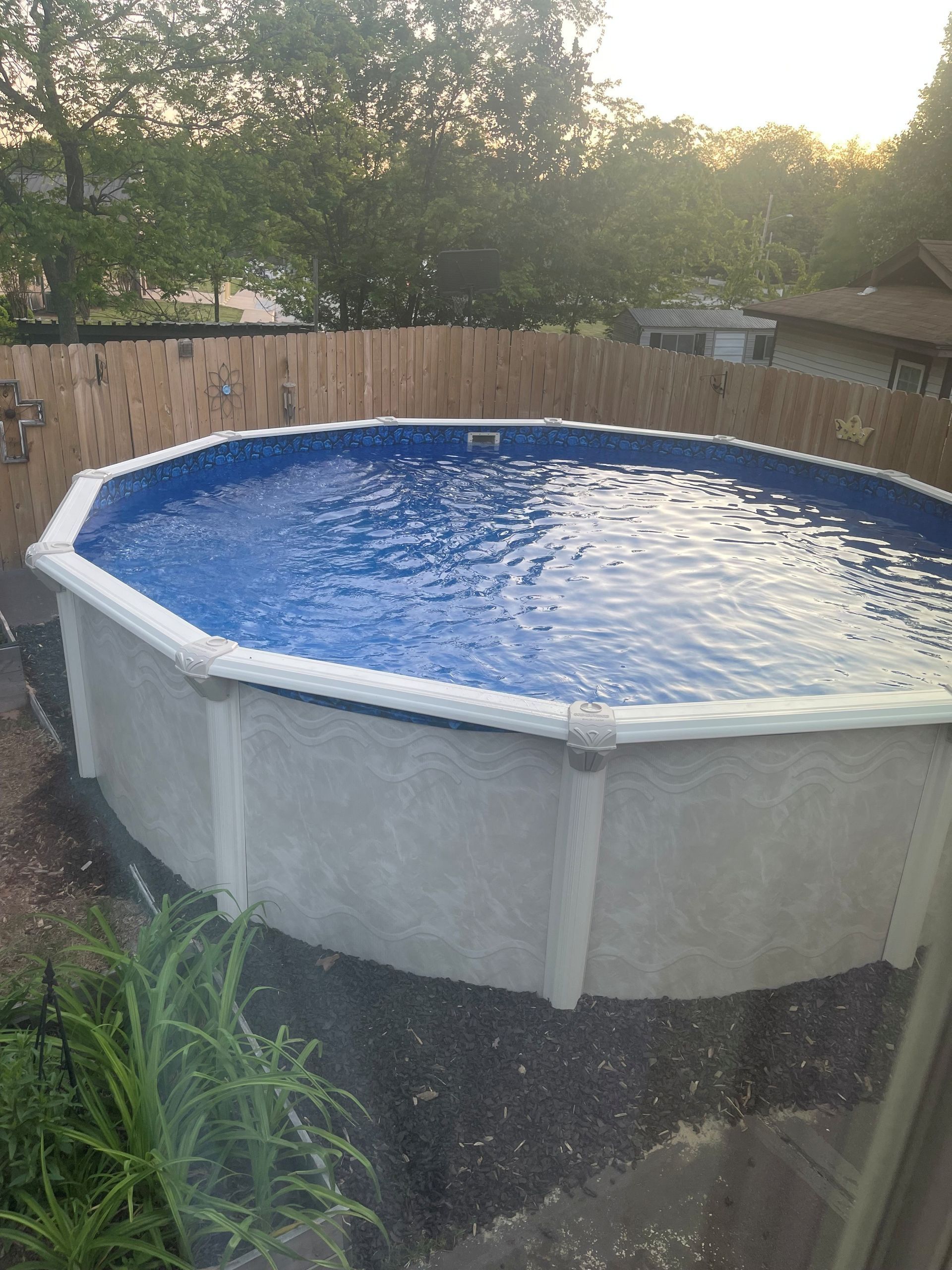 A large swimming pool is sitting in the backyard next to a wooden fence.