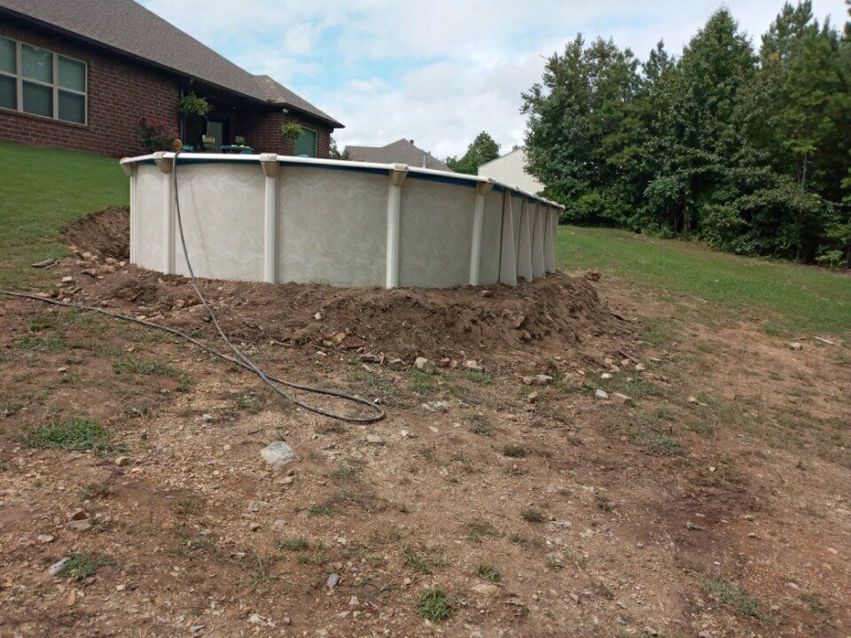 A swimming pool is sitting in the dirt in front of a house.