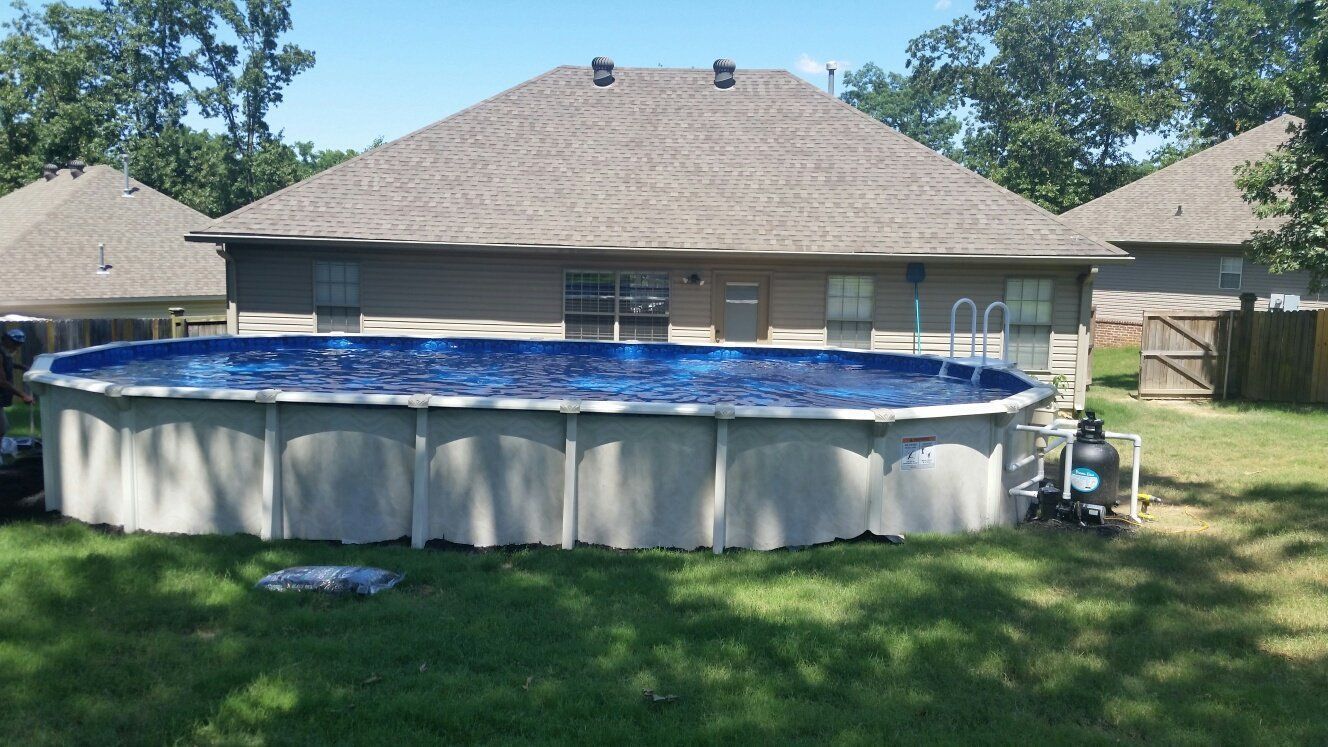 A large swimming pool is sitting in the grass in front of a house.
