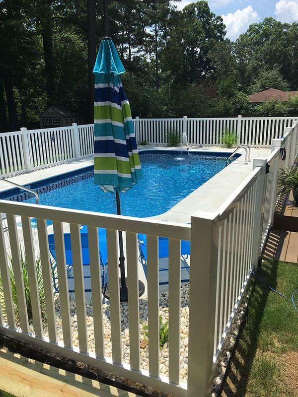A large swimming pool behind a white fence with a blue and green striped umbrella.
