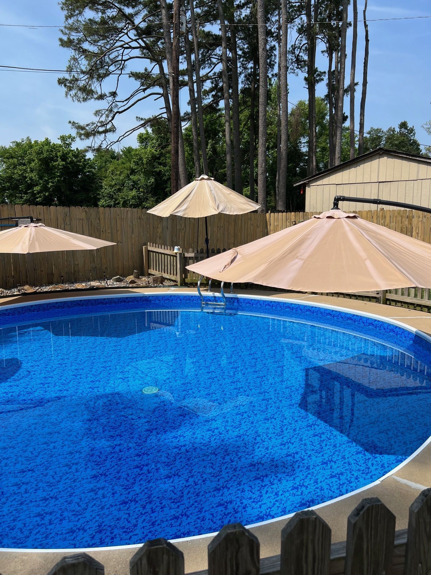 A large swimming pool surrounded by umbrellas and a wooden fence.