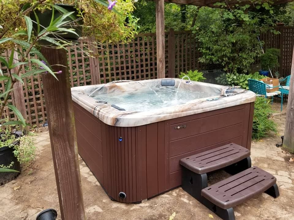 A hot tub is sitting in the sand in a backyard.