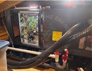 A black HVAC system in an attic; wires and tubing visible. The unit has 