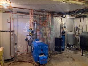 Basement with copper pipes, blue furnace, water heater, tanks, and electrical components.