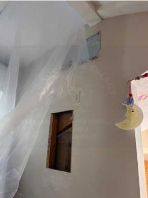 A wall with a rectangular opening, covered with plastic sheeting. A crescent moon mobile hangs nearby.