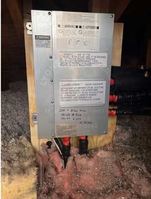 Solar panel system control box mounted on plywood in an attic with insulation.