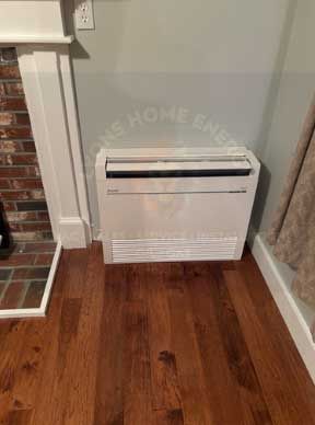 White wall-mounted heating unit on a hardwood floor, next to a fireplace and painted wall.