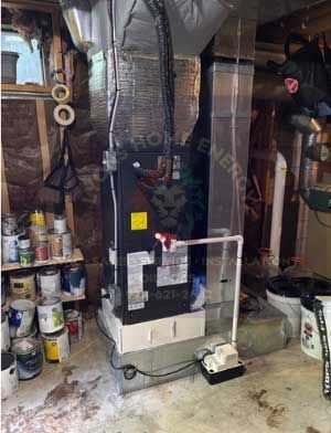 Furnace in basement with ductwork, paint cans on shelf, and a condensate pump.