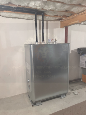 Metal fuel tank with black pipes against a white wall in a basement setting.