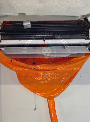 An orange plastic sheet covering a white AC unit being serviced. Black and silver components visible.