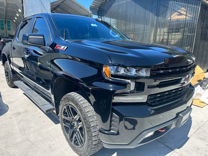 Black pickup truck parked outdoors in sunlight, front-left view with large off-road tires and tinted windows