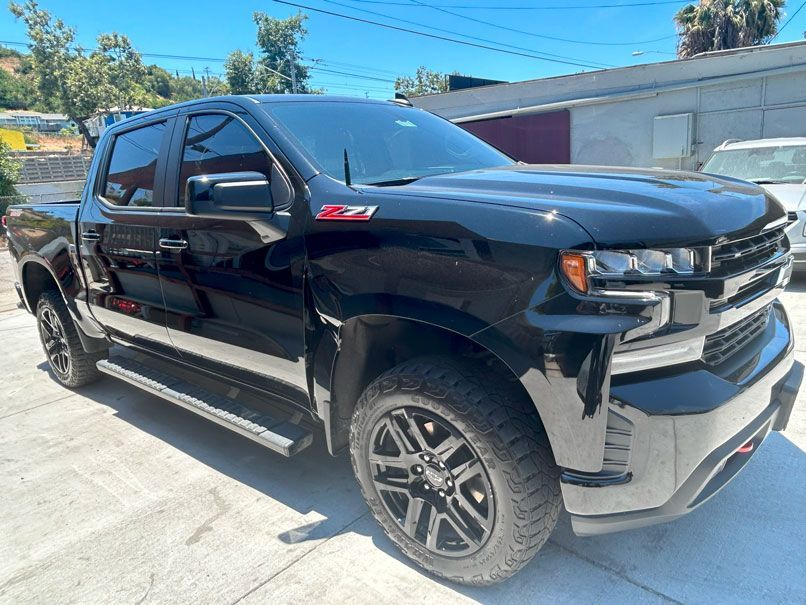 Black Chevrolet Silverado pickup truck parked in a sunny driveway, side view