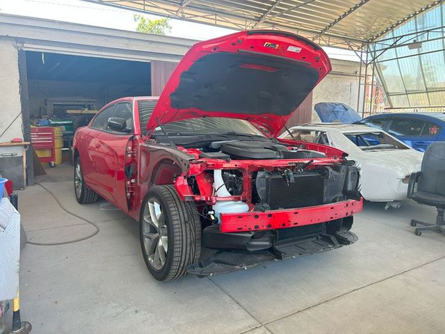 Red car with open hood and damaged front end in a repair garage