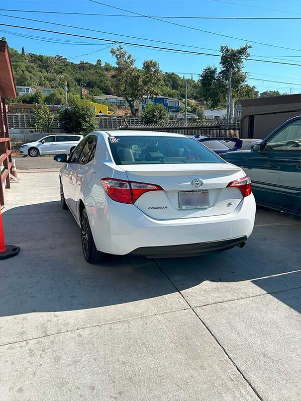 White sedan parked in a driveway beside a black car on a sunny day.