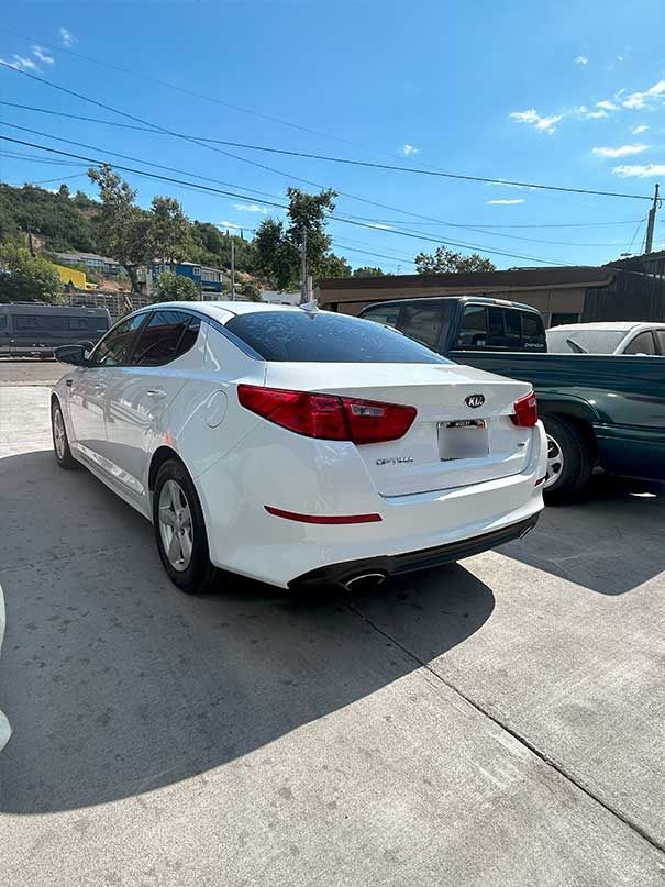 White sedan parked in a sunny lot beside other cars under a blue sky