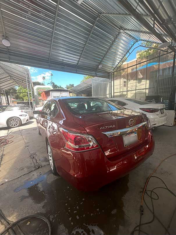 Red sedan parked in a covered car wash with water on the ground