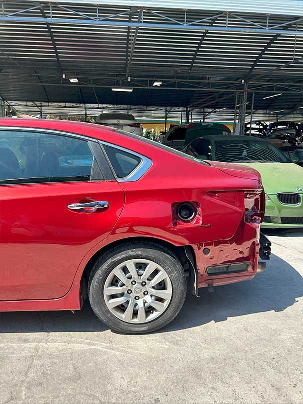 Red sedan with rear-right damage, parked under a covered lot, beside a green car.