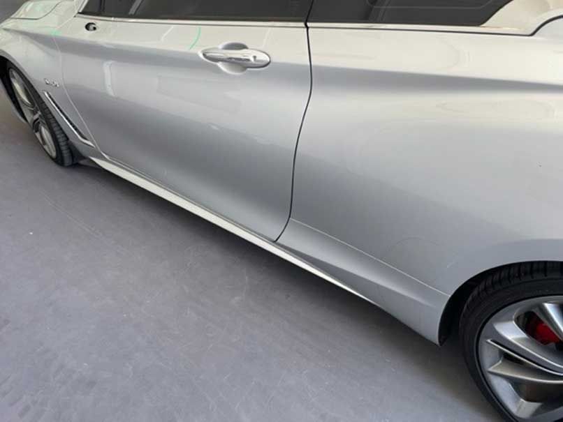 Silver car with a dented lower side panel and visible wheel on a road