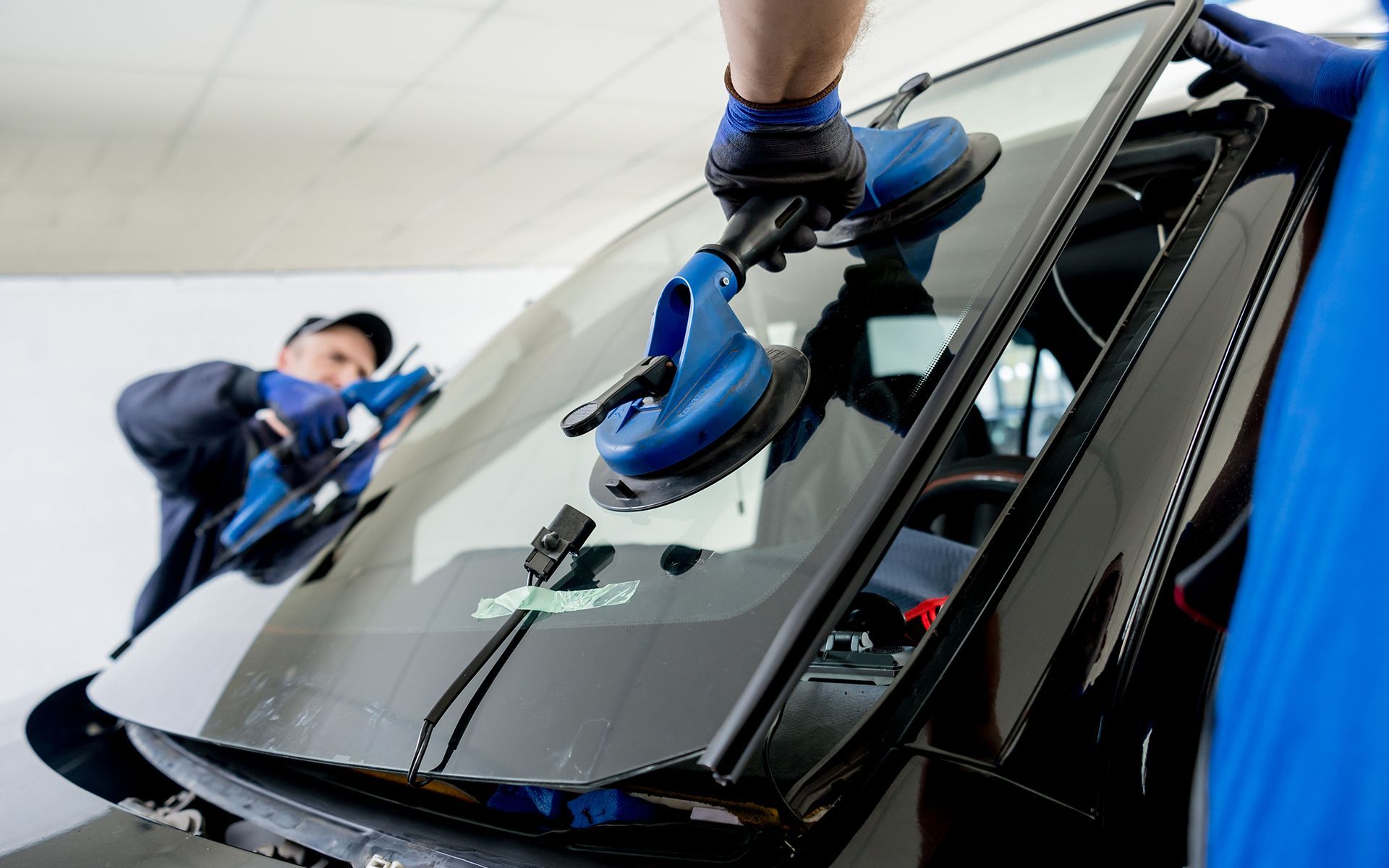Technicians using blue suction tools to repair a car windshield in a workshop
