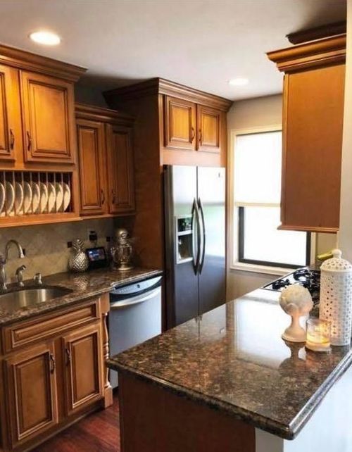 Warm kitchen with wooden cabinets, stainless steel refrigerator, granite island, and hanging wine glass rack.