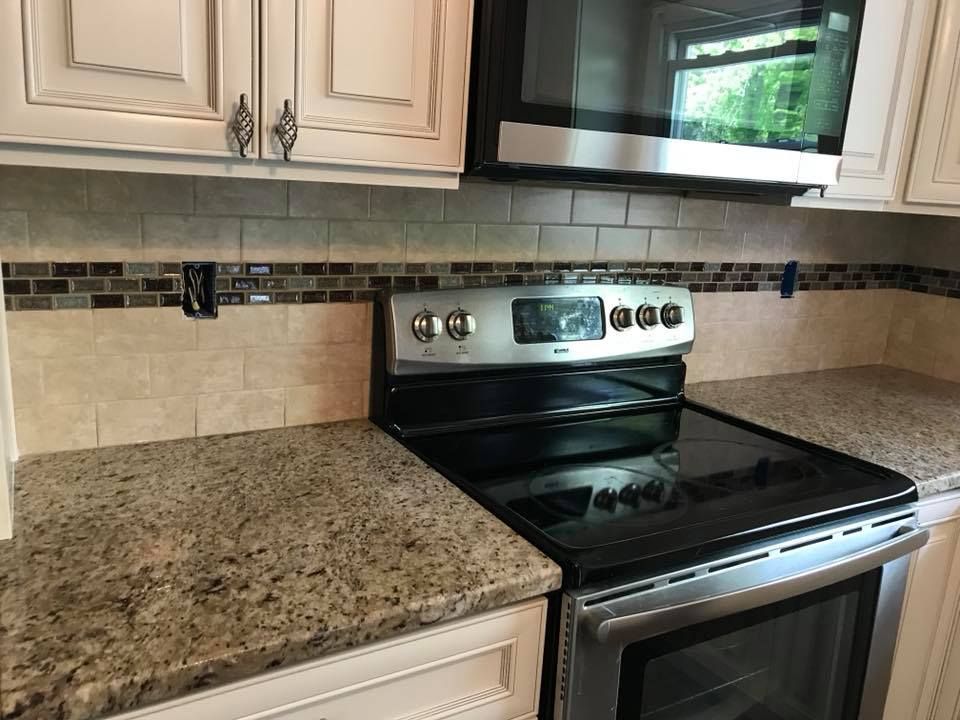 Kitchen with granite countertops, beige tile backsplash, white cabinets, and a black stove beneath a microwave.