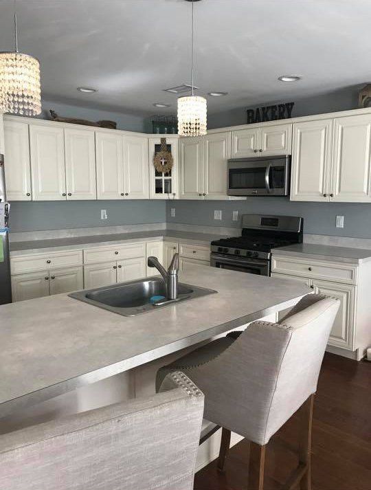 Modern white kitchen with gray backsplash, stainless appliances, and a gray island with two chairs.