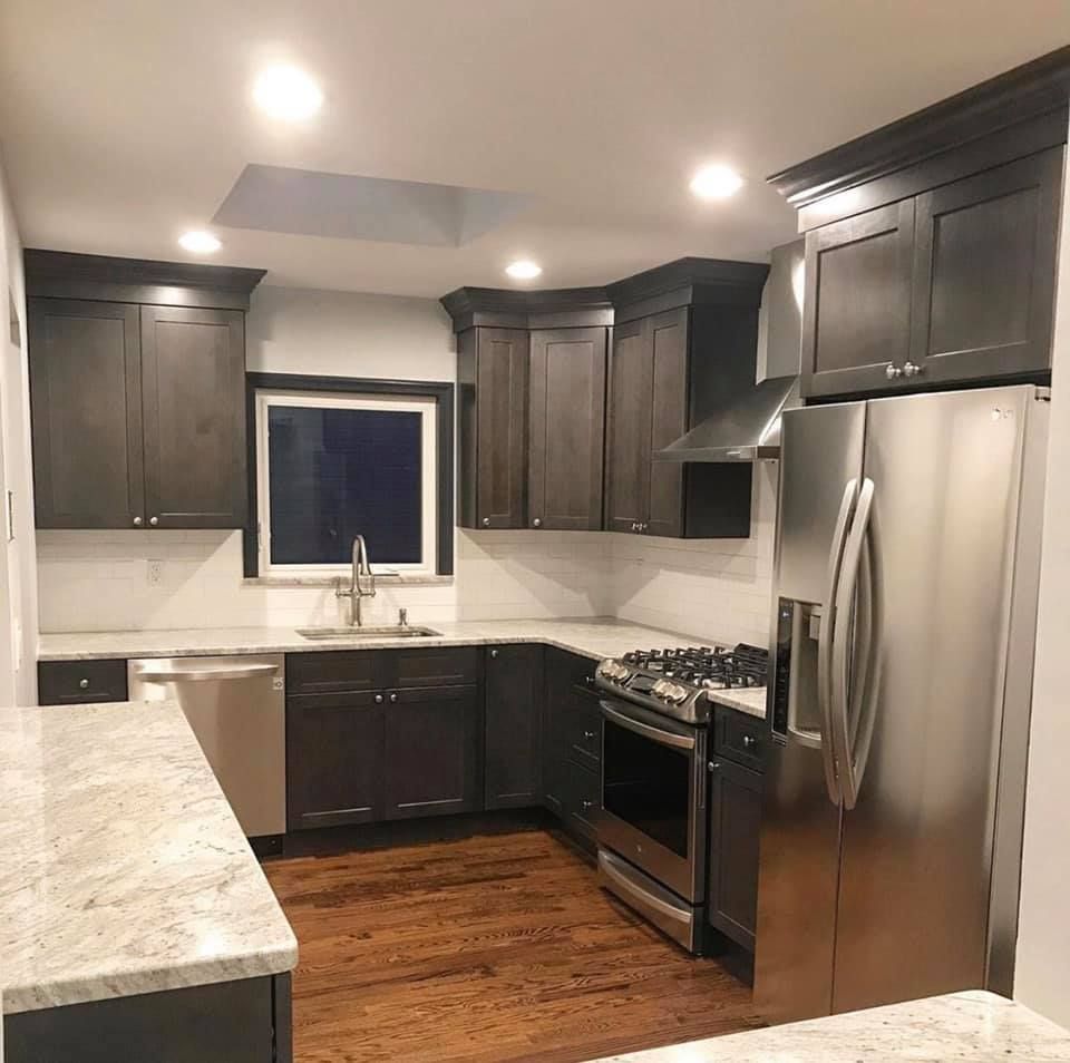 Modern kitchen with dark cabinets, stainless steel appliances, white countertops, and hardwood floor.