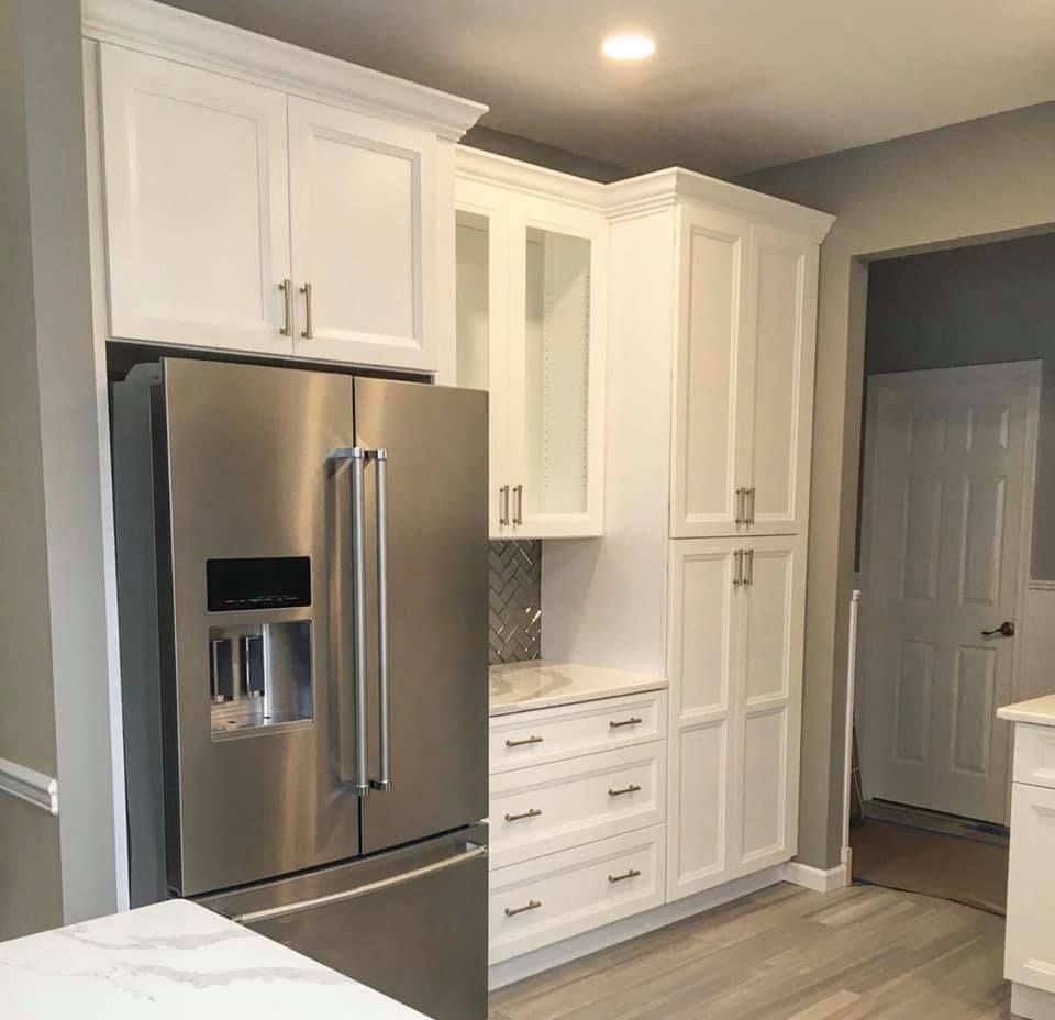 Bright white kitchen with stainless steel fridge, tall cabinets, and light wood flooring.