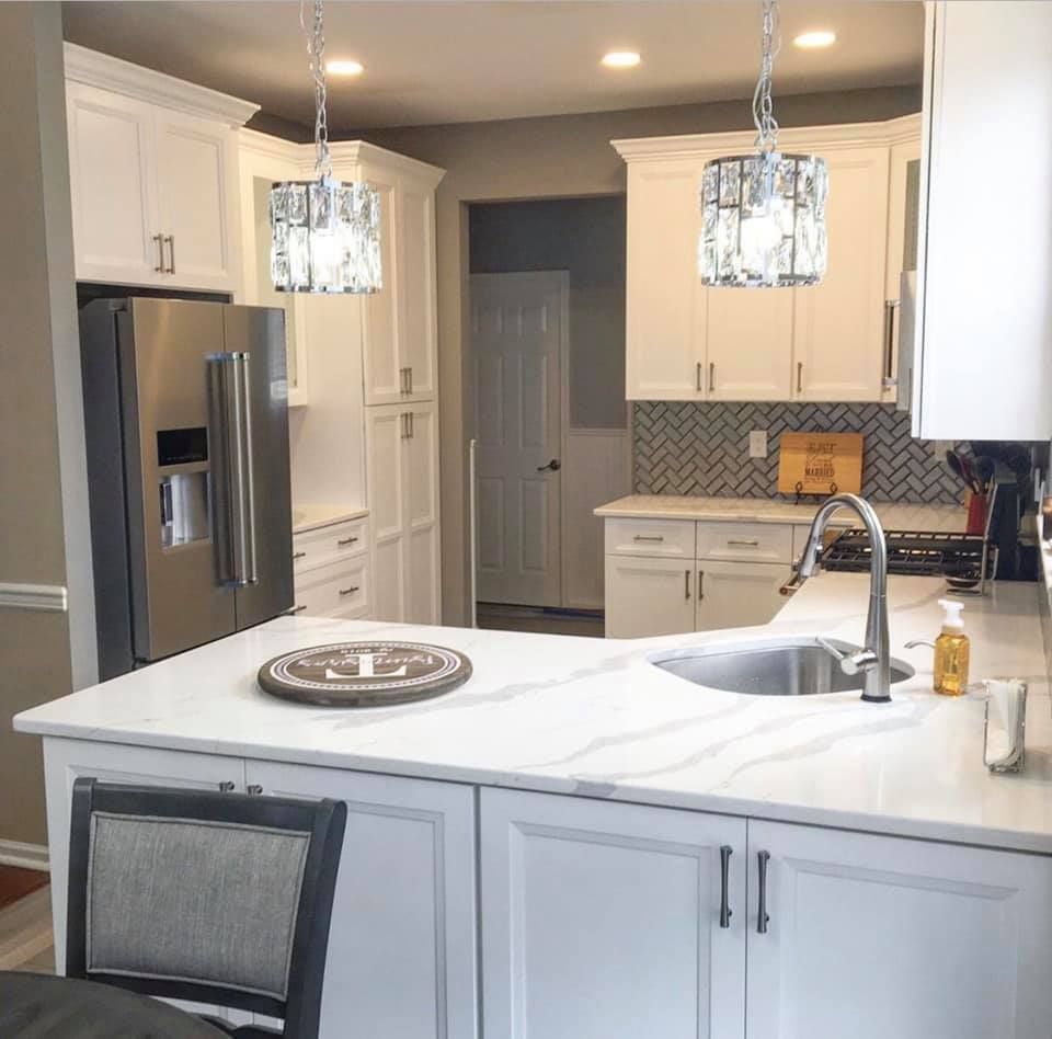 Bright white kitchen with stainless fridge, island sink, pendant lights, and gray cabinets