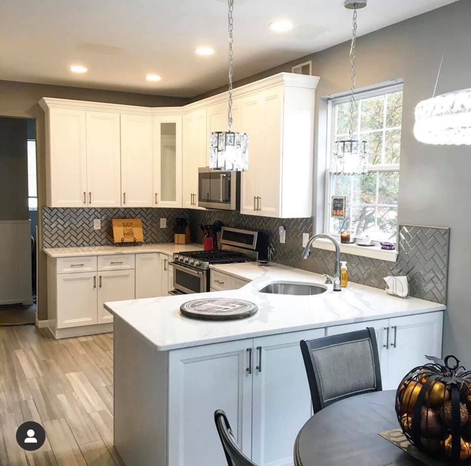 Modern kitchen with white cabinets, gray walls, island sink, pendant lights, and herringbone backsplash.