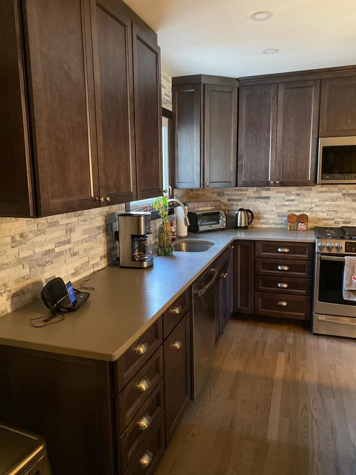 Modern kitchen with dark wood cabinets, stone backsplash, and a gray countertop with small appliances.