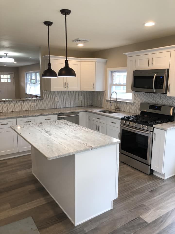 Modern white kitchen with island, pendant lights, stainless steel appliances, and gray wood flooring