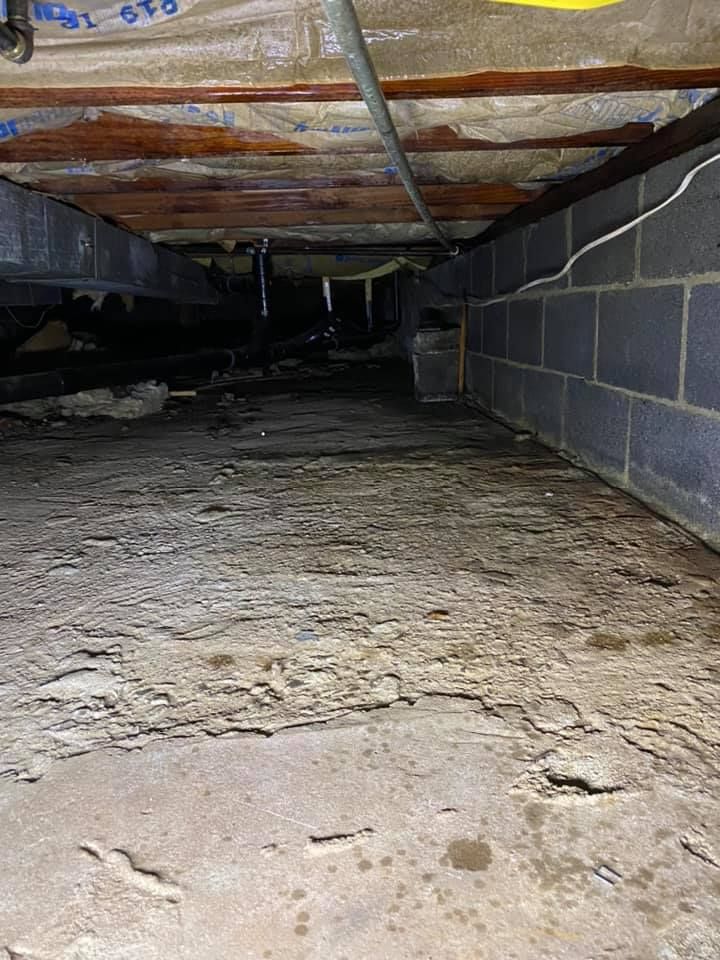 Crawlspace with dirt floor, low wooden beams, and cinder block walls under a house
