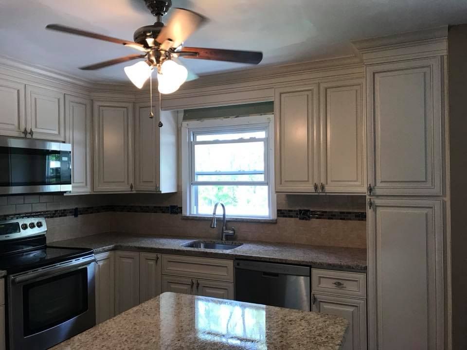 Bright kitchen with cream cabinets, black appliances, a window over the sink, and a ceiling fan above.