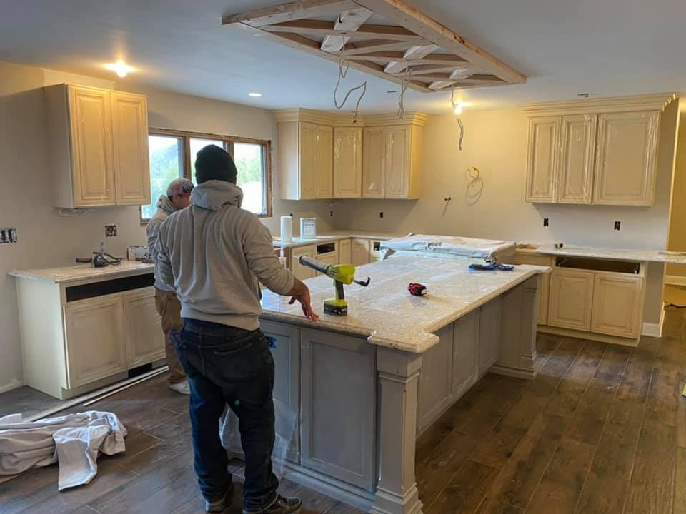 Two workers renovating a bright kitchen with a large island and light wood cabinets