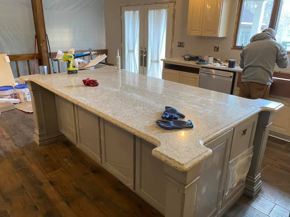Kitchen with a large white island countertop and a person working at the sink in the background.