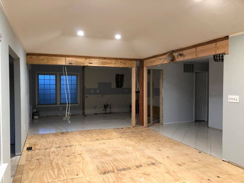 Empty home interior with exposed beams, unfinished floor, and kitchen visible in the background