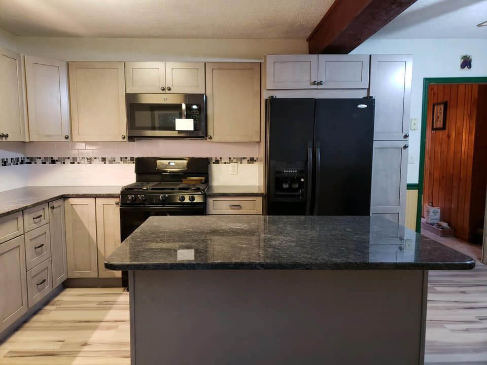 Modern kitchen with cream cabinets, black appliances, granite island, and light wood floor