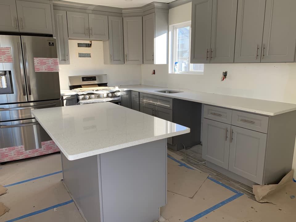 New kitchen with gray cabinets, stainless appliances, and a white island countertop under construction