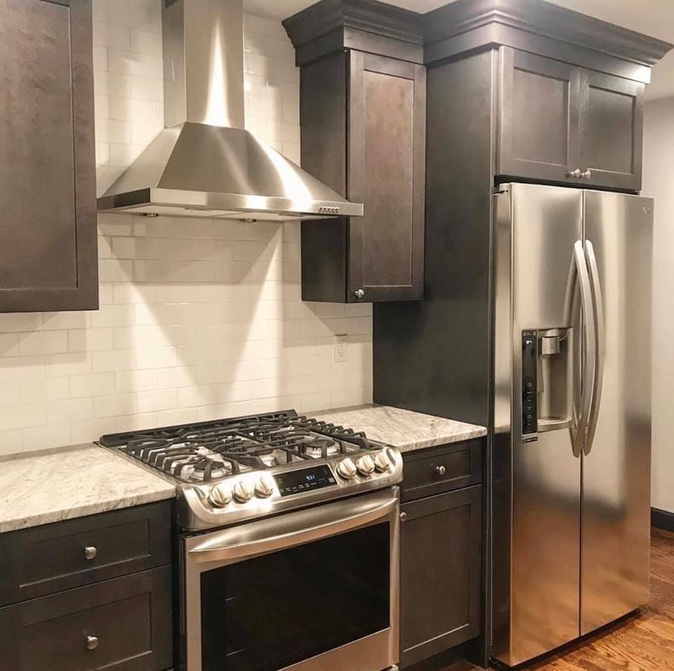 Modern kitchen with dark wood cabinets, stainless steel stove, range hood, and refrigerator under warm lighting