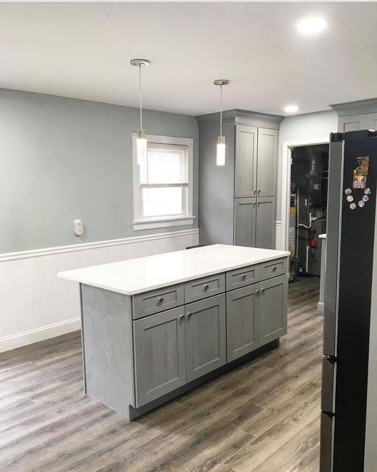 Modern kitchen with gray island, white counters, pendant lights, and wood-look flooring.
