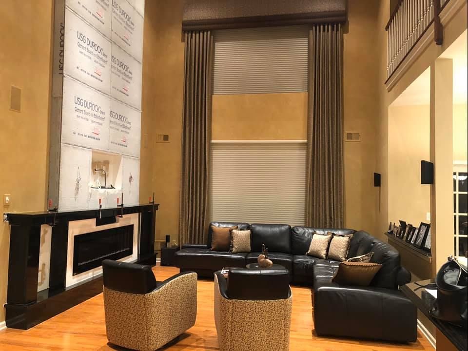 Modern living room with black leather sofas, patterned chairs, fireplace, and tall windows