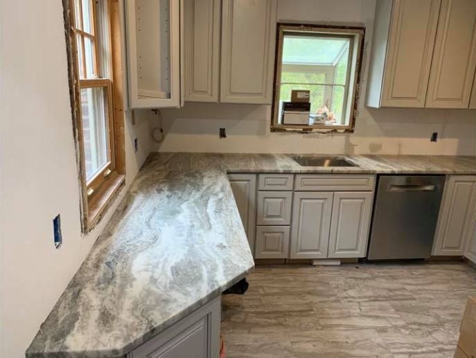 Bright kitchen with white cabinets, gray countertops, wood-look floor, and a window over the sink.