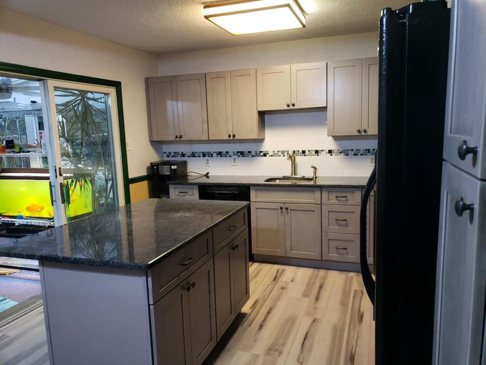 Modern kitchen with light wood cabinets, dark island countertop, and black appliances