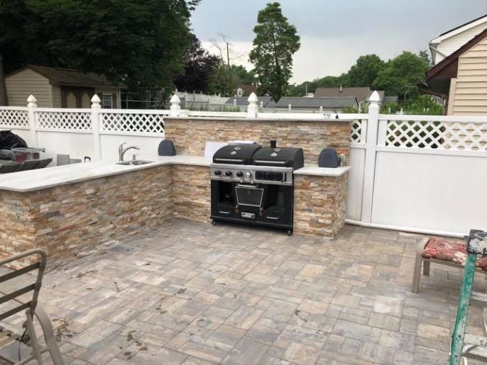 Backyard patio with stone pavers, built-in grill, and white lattice fence.