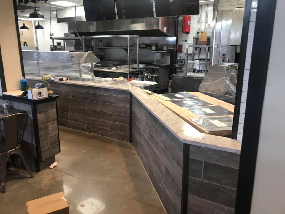 Empty restaurant counter with wood paneling, stainless kitchen equipment, and a glass display case